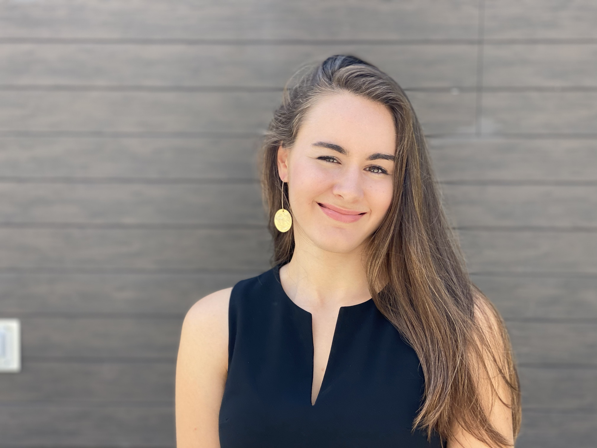 Photo of Allie Reed, a woman with long hair in front of a grey brick wall. 